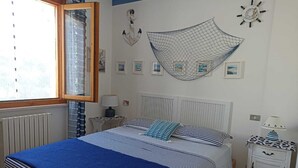 Un dormitorio con una cama, una mesita de noche, una lámpara, una ventana y adornos en la pared.