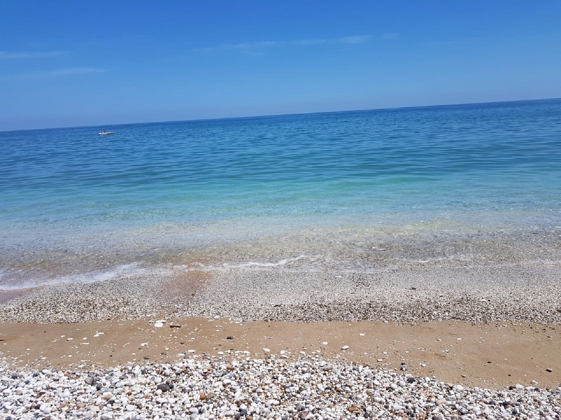 Une plage de galets avec une eau claire et un bateau visible au loin.
