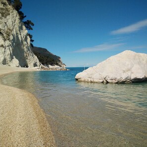 A beach with clear shallow waters, a rocky cliff, and a large white rock formation. - Passione Marinara Three-room apartment near the sea terrace parking space-Marcelli center (Numana)