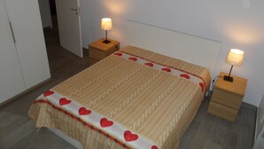 A neatly made bed with a patterned bedspread and heart-shaped pillows, flanked by two bedside tables with lamps.