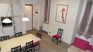 A dining area with a table and chairs, a kitchen in the background, a red chair, and a sofa with a colorful blanket.