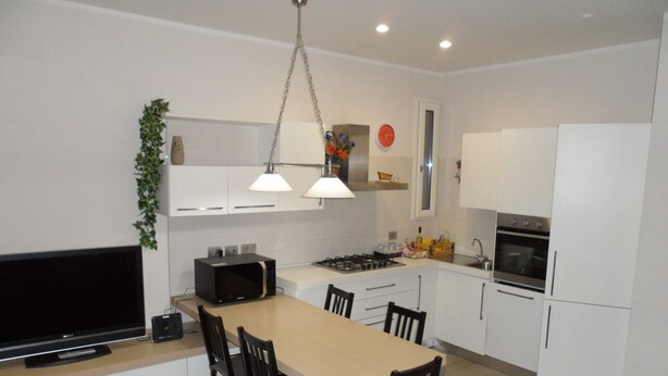 A modern kitchen with white cabinets, a central island with chairs, a microwave, a gas stove, and a flat-screen TV.