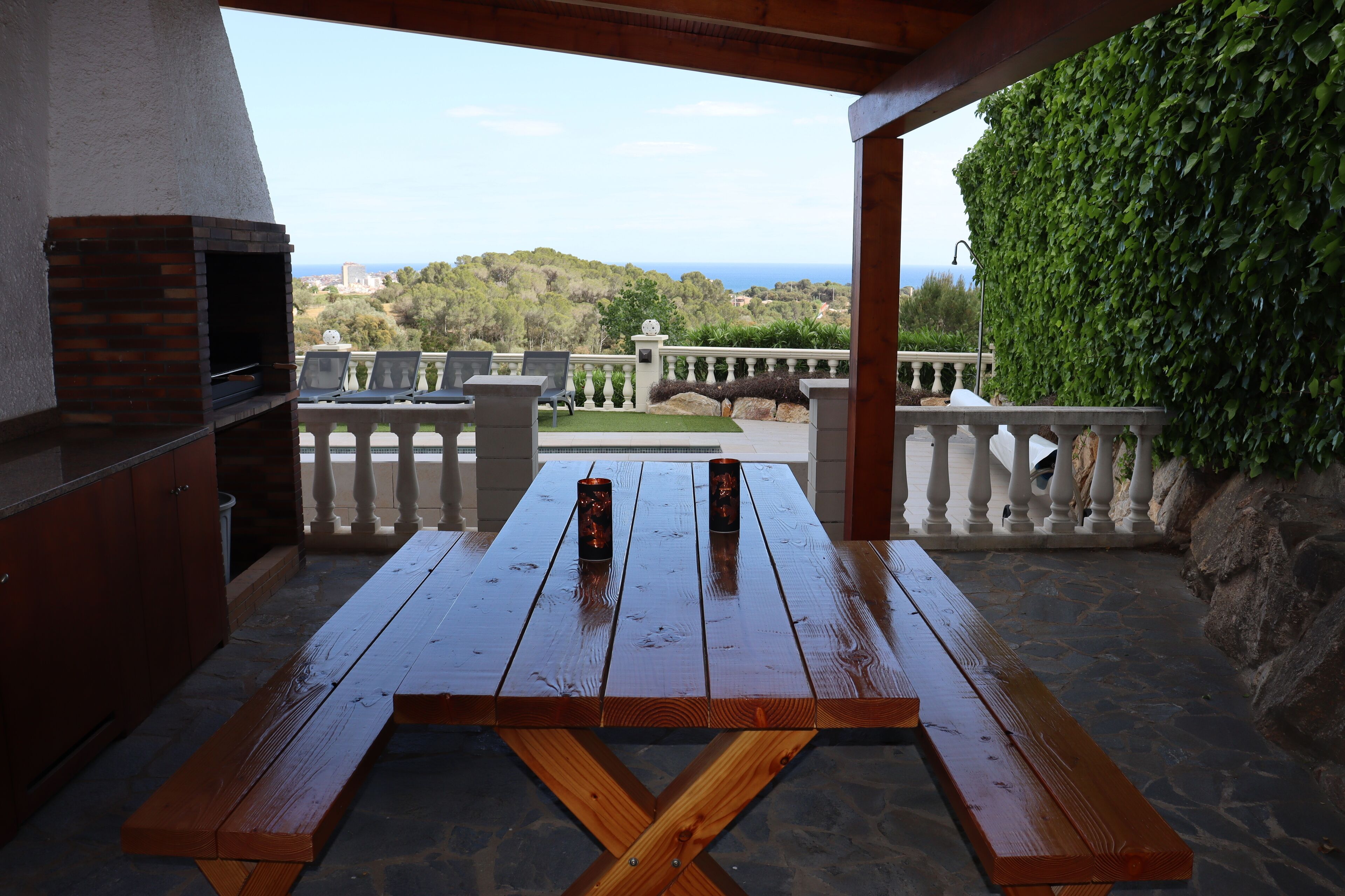 An outdoor patio with a wooden table, benches, and a brick oven.