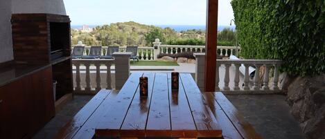 An outdoor patio with a wooden table, benches, and a brick oven.