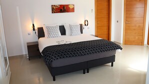 Un dormitorio moderno con una cama grande, lámparas de noche, aire acondicionado montado en la pared y una puerta de madera.