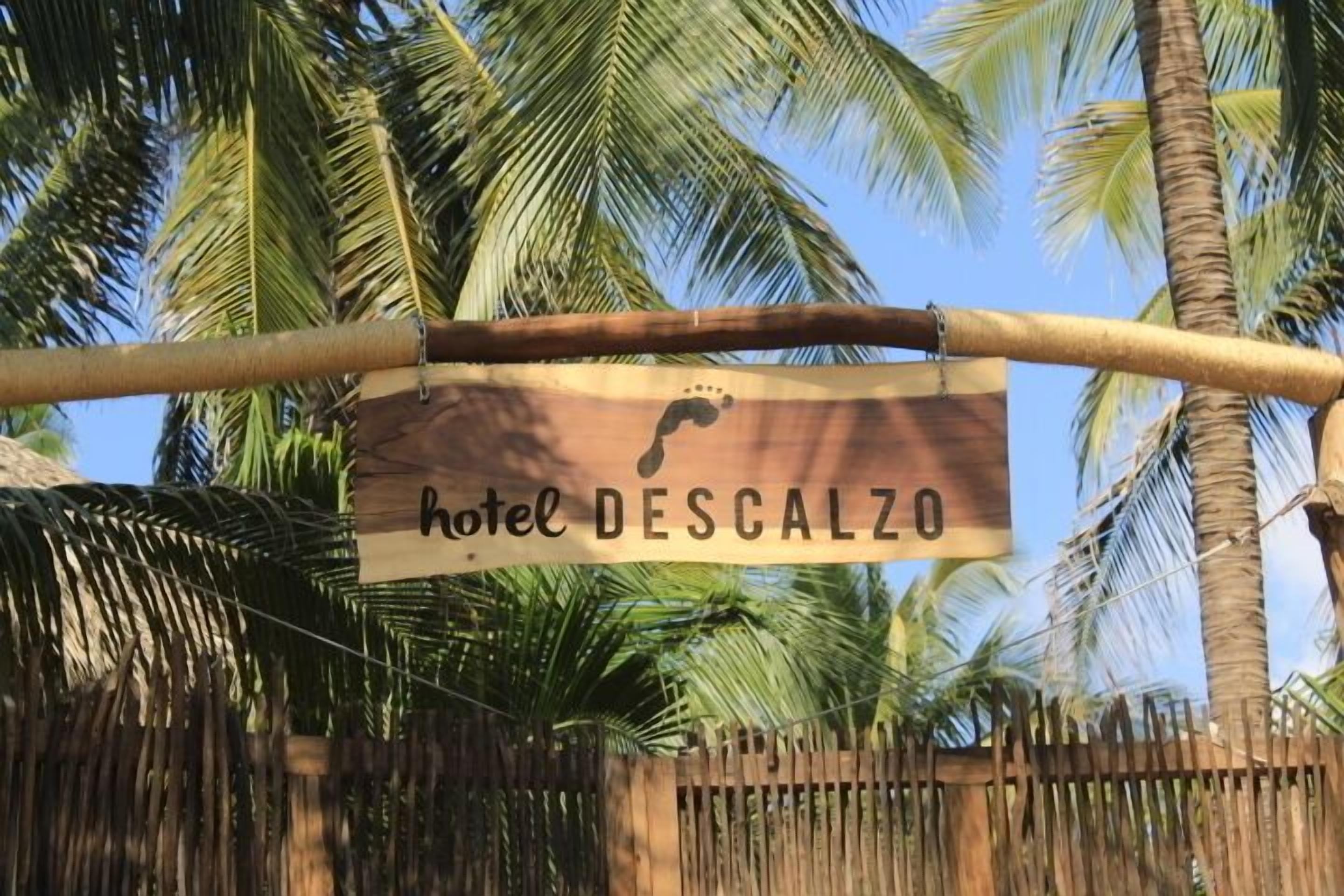 Een bordje voor 'Hotel DESCALZO' met een palmbomenachtergrond.
