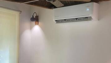 Habitación de hotel con dos camas, un escritorio de madera con artículos de aseo, un ventilador de techo y un equipo de aire acondicionado.