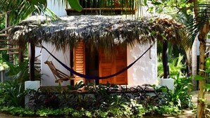 A small, thatched-roof hut with a wooden door, surrounded by lush greenery and a hammock. - Hotel Descalzo (San Pedro Pochutla)