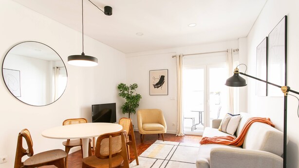 A modern living room with a dining area, a sofa, a TV, and a large window.