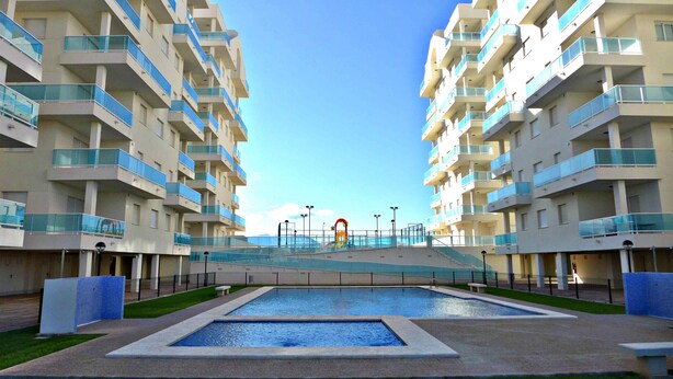 Un moderno edificio de apartamentos con piscina central, varios balcones y cielo despejado.