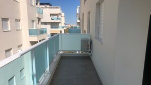 Un balcón estrecho con barandilla de metal, piso de baldosas y vista a edificios vecinos.