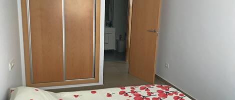 Camera da letto con un letto, un armadio in legno e un bagno visibile attraverso una porta aperta.