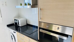 Una cocina moderna con microondas integrado, tostadora y horno. Hay una lavadora y un armario de madera con un estante superior.