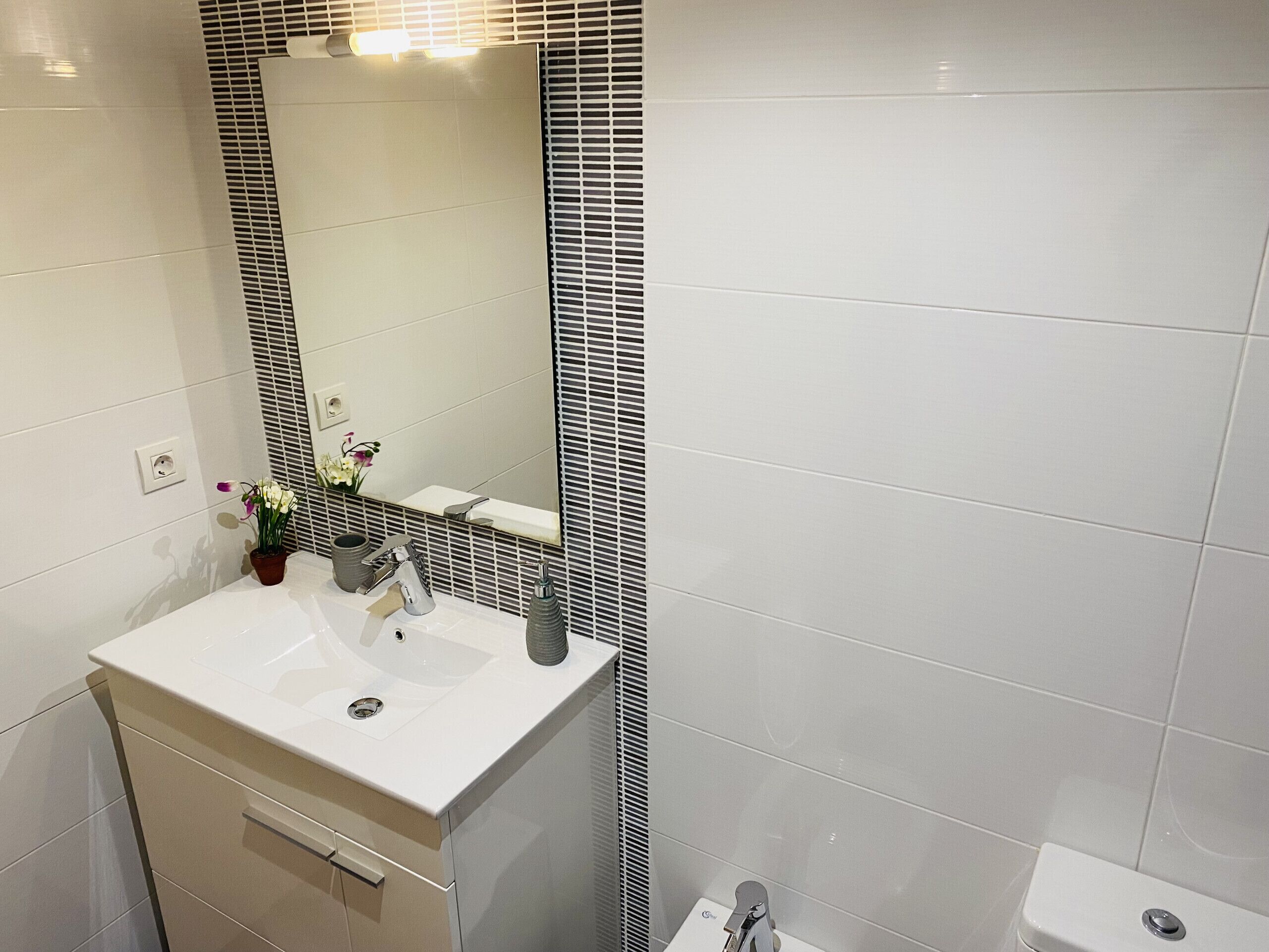 A modern bathroom with a white sink, mirror, and toilet.