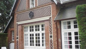 Ein zweistöckiges Gebäude mit Ziegelaußenwand, weißen Doppeltüren und einem kleinen Balkon mit Gitterveranda.