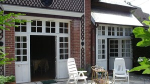 Ein Backsteinhaus mit großer offener Tür und Fenstern, einem kleinen Tisch mit Stühlen und einem Blumentopf.