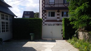 Ein mit Kopfsteinpflaster belegter Innenhof mit einem vergitterten Eingang, einer Mülltonne und einer Hecke.
