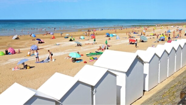 Ein Strand mit weißen Strandhütten und Menschen, die Sand und Meer genießen.