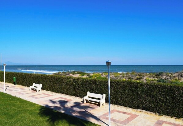 A coastal walkway with benches and a lamppost, leading to the ocean.