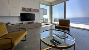 Un salon moderne doté d’un grand téléviseur, de sièges confortables, d’une table basse en verre et offrant une vue sur l’océan.