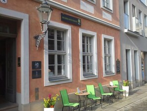 A building with a sign reading "Hotel". There are outdoor seating areas with green chairs and tables.