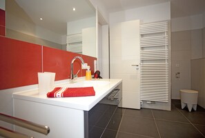 A modern bathroom with a white sink, red accent wall, and a towel rack.