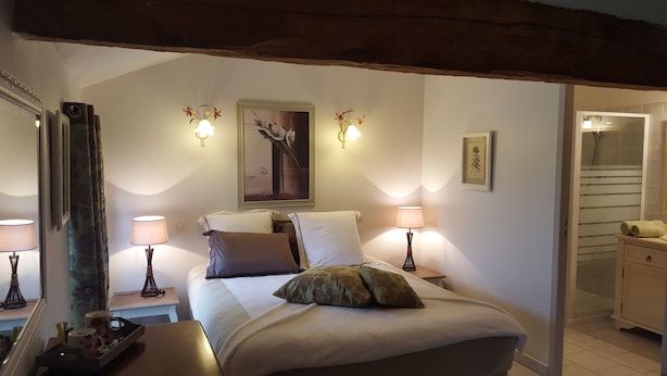 A bedroom with a bed, two bedside tables, lamps, a mirror, and a painting on the wall.