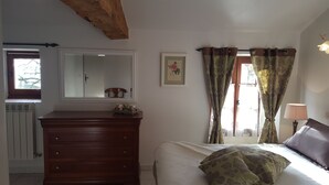A bedroom with a wooden dresser, a bed with floral-patterned pillows, a framed picture on the wall, and a window with curtains.
