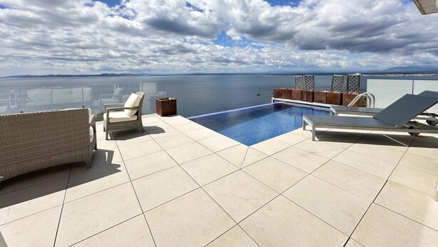 Une terrasse sur le toit avec une piscine, des chaises longues et une vue sur la mer.