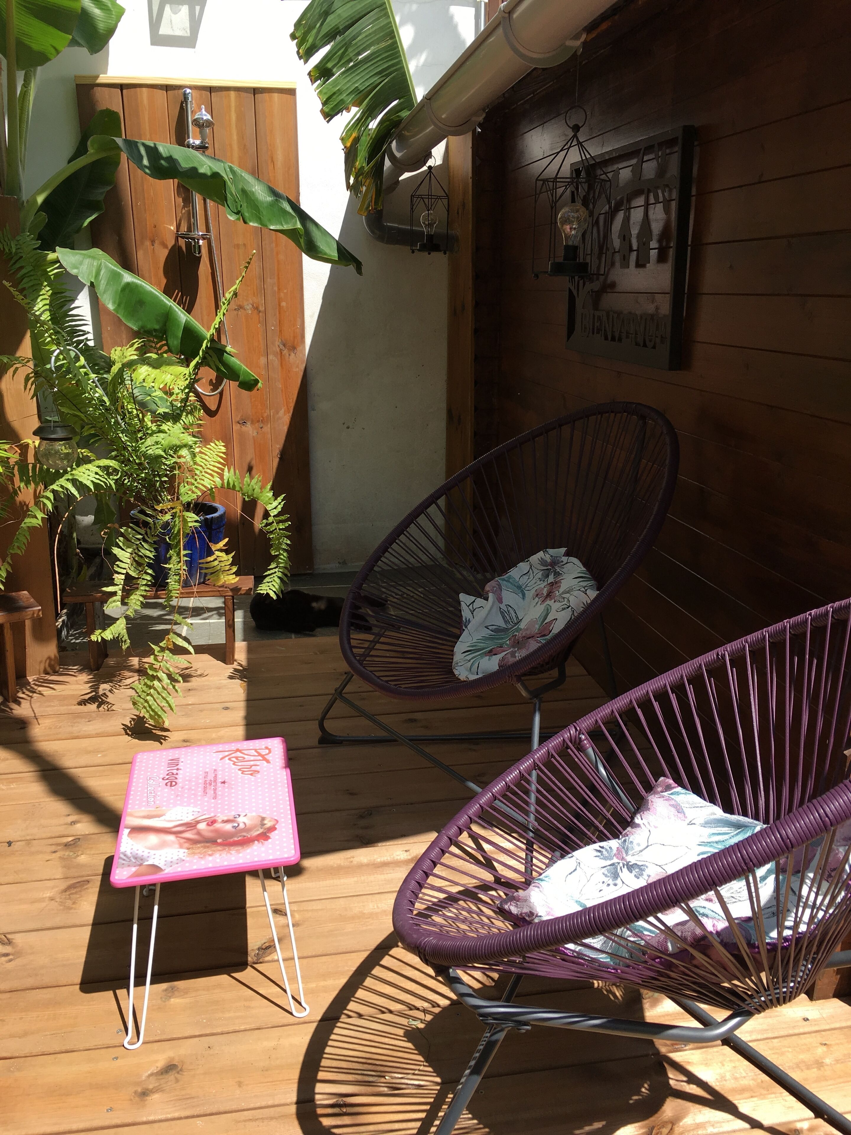 Een houten terras met twee paarse stoelen, een kleine tafel en een bord dat een retro vintage collectie aanprijst.