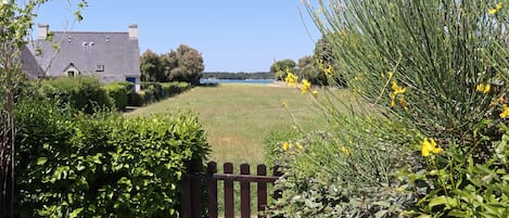 A rural landscape with a house, a grassy field, and a wooden gate.