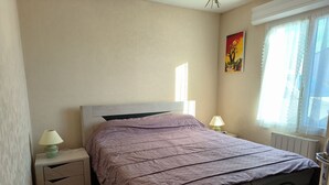 Un dormitorio con cama, mesitas de noche, ventana con cortinas y un radiador.