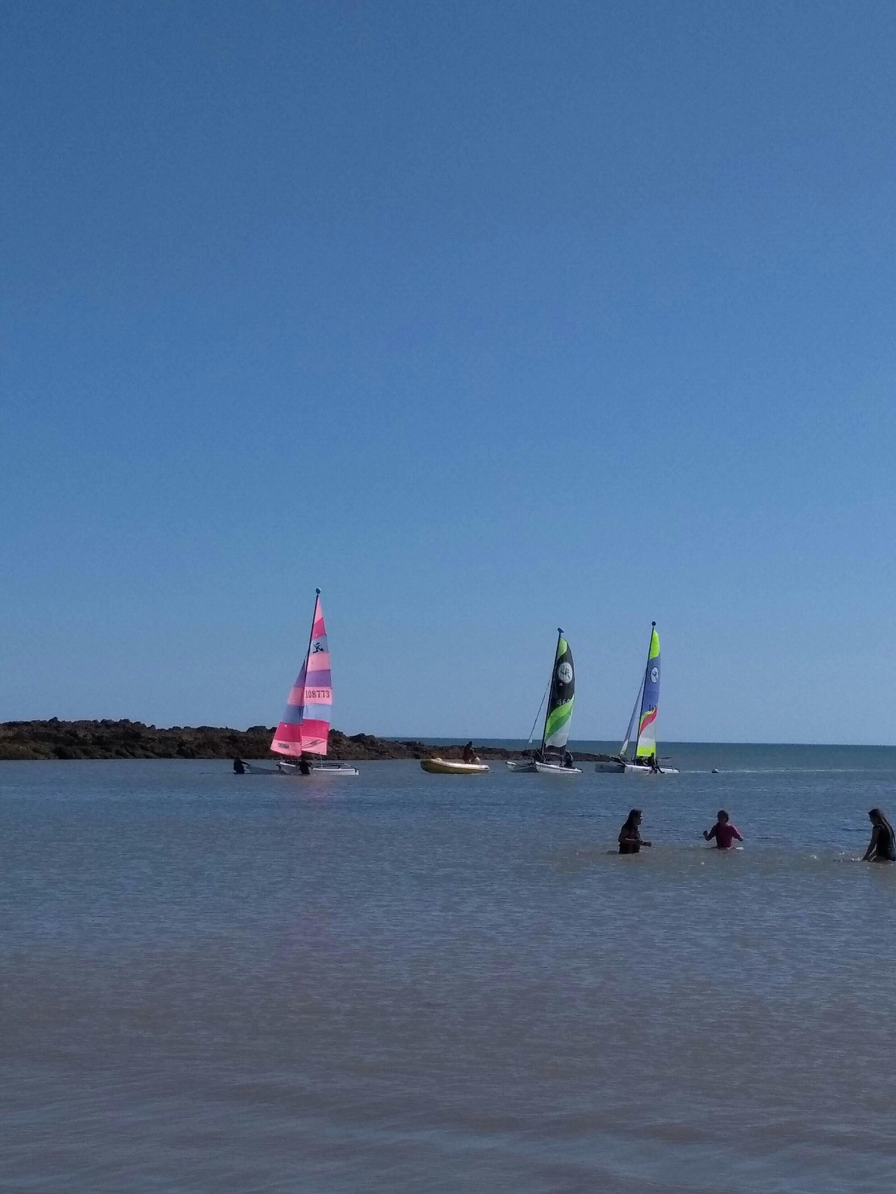 A beach scene with sailboats and people in the water.