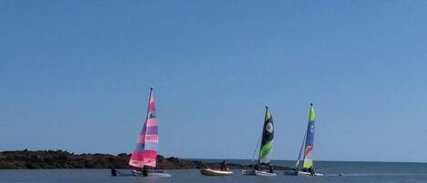 A beach scene with sailboats and people in the water.