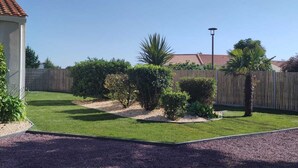 Un patio trasero bien cuidado con césped, arbustos variados, una palmera y una valla de madera.