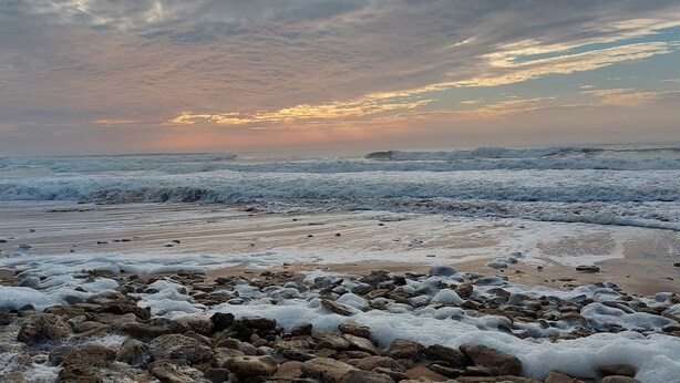 Una playa con olas, rocas y un atardecer.