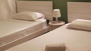 Een hotelkamer met twee bedden, elk voorzien van witte lakens en kussens. Daartussen bevindt zich een klein nachtkastje met een lamp.