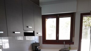 Een moderne keuken met donkere kastjes, een inbouwoven, een koffiezetapparaat en een raam met jaloezieën.