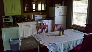 A compact kitchen with white cabinets, a microwave, a stove, and a refrigerator. There is a table with a tablecloth and two chairs. A trash bin is visible near the kitchen entrance. - Relaxing getaway in a peaceful spacious setting (Long Beach)