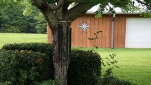 A tree with a compass mounted on its trunk, a wooden building with a garage door, and a well-maintained lawn. - Relaxing getaway in a peaceful spacious setting (Long Beach)