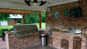 An outdoor kitchen with a grill, sink, and trash can, surrounded by a brick wall and wooden accents. - Relaxing getaway in a peaceful spacious setting (Long Beach)