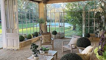 A covered patio with seating, potted plants, and a view of a garden.