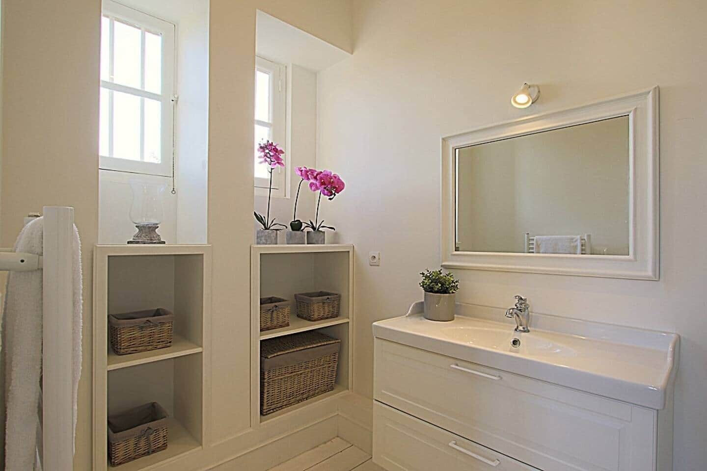 A bathroom with a large mirror, white cabinets, wicker baskets, and potted plants.