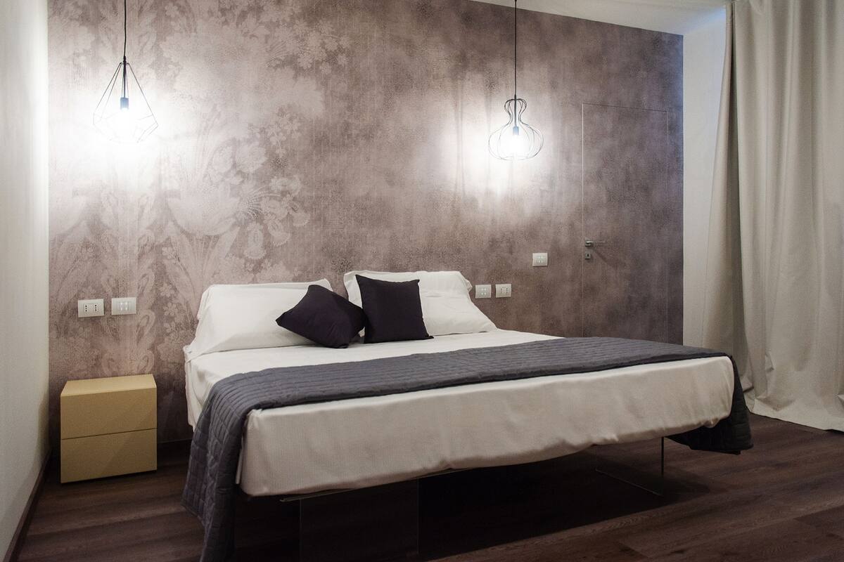 Un dormitorio moderno con una cama, dos lámparas colgantes, una mesita de noche y suelo de madera.