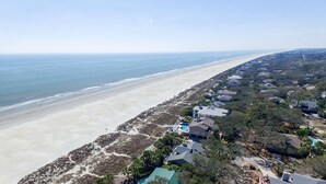 An aerial view of a coastal residential area with houses along the beach, a clear sky, and a visible ocean.