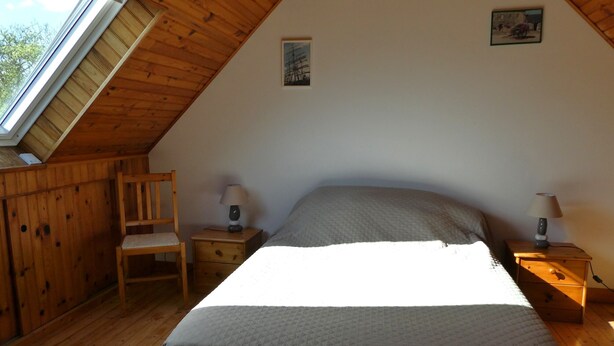 A bedroom with a sloped ceiling, a bed, two bedside tables with lamps, a wooden chair, and a small picture on the wall. - The stable, quiet house in the bay of Dournenez (Quéménéven)