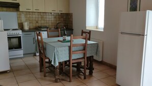 A small kitchen with a dining table, chairs, a refrigerator, a stove, and a window. - The stable, quiet house in the bay of Dournenez (Quéménéven)