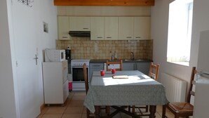 A compact kitchen with white cabinets, a dining table with a tablecloth, and a window providing natural light. - The stable, quiet house in the bay of Dournenez (Quéménéven)