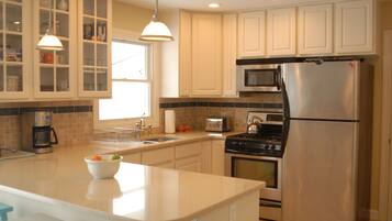A modern kitchen with white cabinets, stainless steel appliances, and a central island with a bowl of fruit.