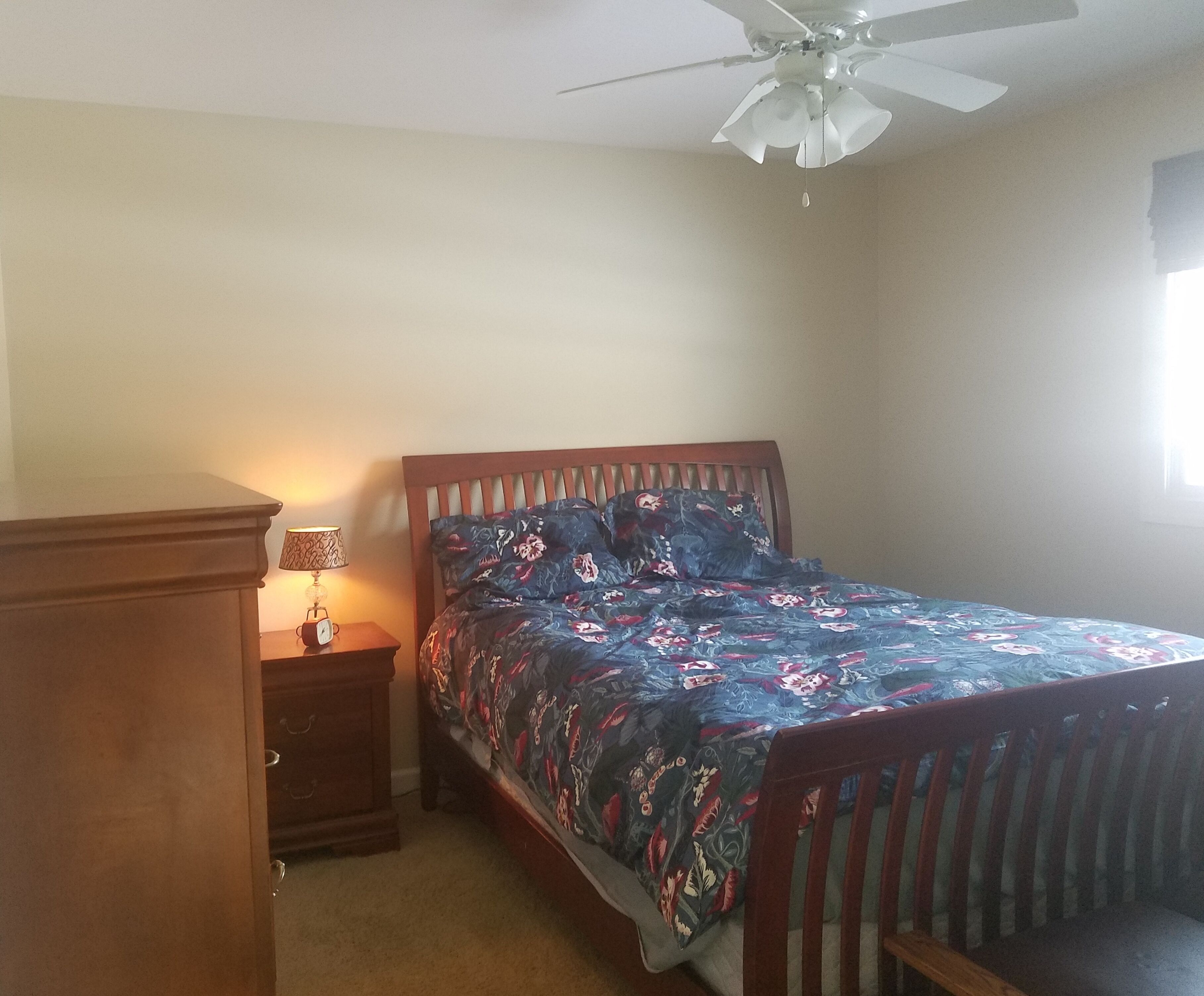 Ein Schlafzimmer mit einem Bett, einem Nachttisch, einer Lampe und einem Deckenventilator.